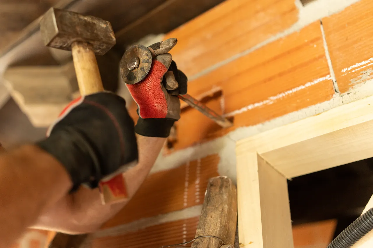 Handyman using hammer and chisel on a brick wall in New York